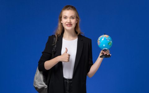 front-view-female-student-black-jacket-wearing-backpack-holding-little-globe-blue-wall-school-college-university-earth
